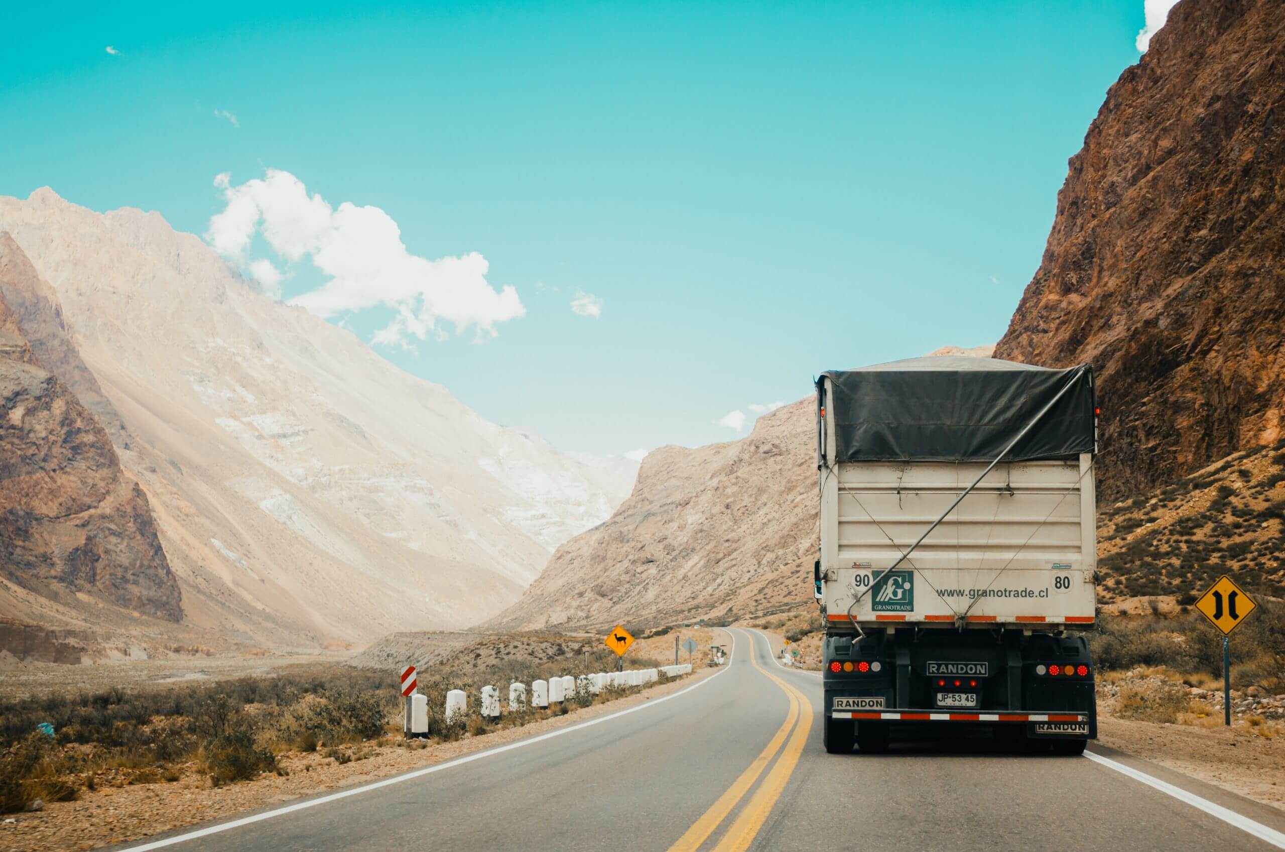 A truck driving down the road near mountains.